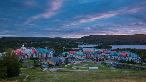 Panoramic sunset view of Tremblant Resort pedestrian village with Lake Tremblant and mountains in the background.