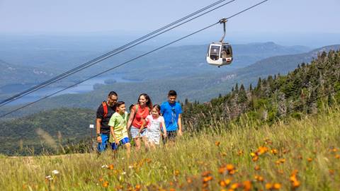 Family hiking on a grassy trail at Tremblant Resort with a panoramic view of the mountains and the panoramic gondola overhead.