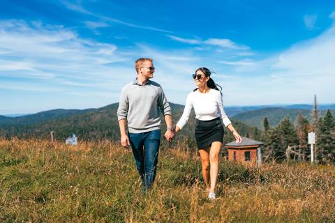 A couple walking on a grassy mountain summit at Tremblant with forest and hills in the background.