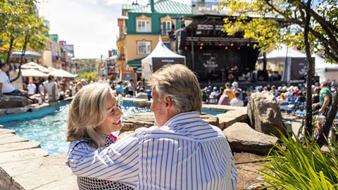 A couple enjoying an outdoor concert near a water feature in the Tremblant pedestrian village during summer.