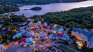 Aerial evening view of the Tremblant pedestrian village buildings and Lake Tremblant surrounded by forest.