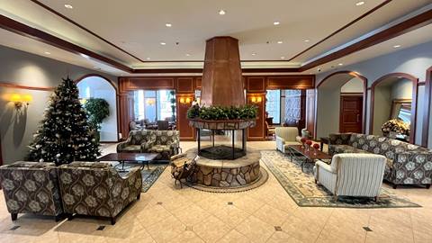 spacious lobby of Sommet des Neiges in Mont-Tremblant, featuring a central stone fireplace, patterned armchairs, and a decorated Christmas tree.