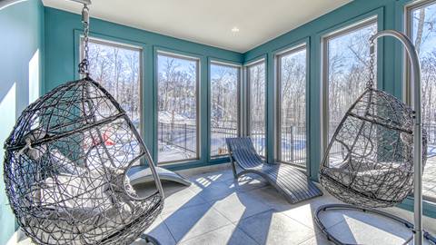 A sunlit indoor lounge area at the Verbier vacation rental with hanging egg chairs and floor-to-ceiling windows overlooking a winter landscape.