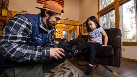 A Ski Butlers technician fitting a young girl with snowboard boots inside a Mont-Tremblant vacation rental.