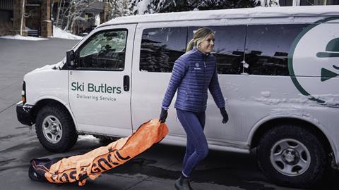 A Ski Butlers delivery van parked outside with a staff member unloading a snowboard bag for a guest.