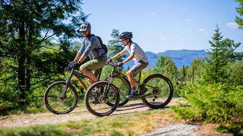 Père et fils en vélo de montagne sur un sentier en forêt, avec vues panoramiques le long des sentiers de vélo de Tremblant