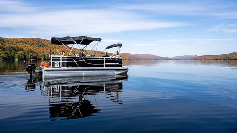 Pontoon boat floating on a calm lake with autumn trees in the background at Mont Tremblant boat rentals