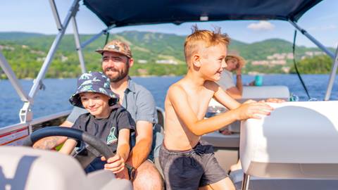Bateau ponton voguant sur un lac paisible, bordé d’arbres aux couleurs d’automne, avec Tremblant à l’arrière-plan – location de bateaux Tremblant