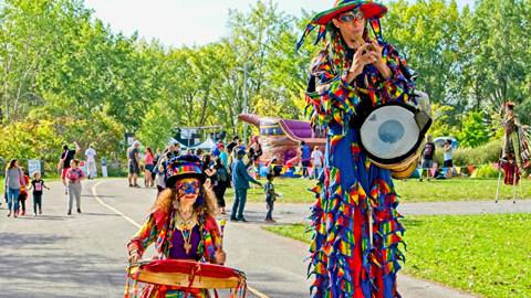 Two street performers in costumes playing drums and woodwind instruments in a park at Mont-Tremblant.