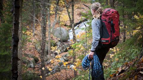 Woman in forest holding climbing rope with a large backpack during a wilderness survival class in Tremblant