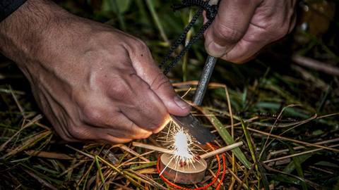 Close-up of hands using a fire starter to create sparks on dry grass while learning safe fire starting techniques during wilderness survival training in Tremblant