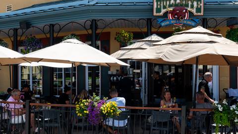 Vue extérieure du restaurant Bullseye Saloon & Grillades dans le village piétonnier de Mont-Tremblant, avec une terrasse munie de parasols beiges.