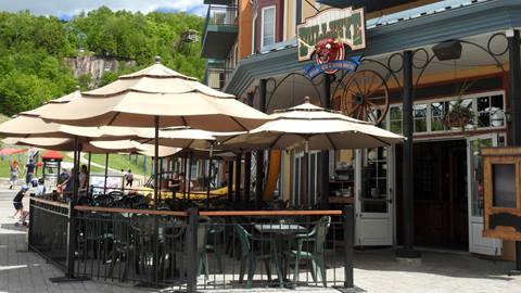 Exterior view of the Bullseye Saloon & Grillades restaurant in the Mont-Tremblant pedestrian village featuring a patio with beige umbrellas.